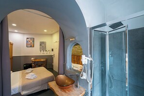 Ein modernes Hotelzimmer mit einem Bett, einem Holzinlay, einem großen Spiegel, einer Dusche und einem kleinen Tisch mit einer Schale.