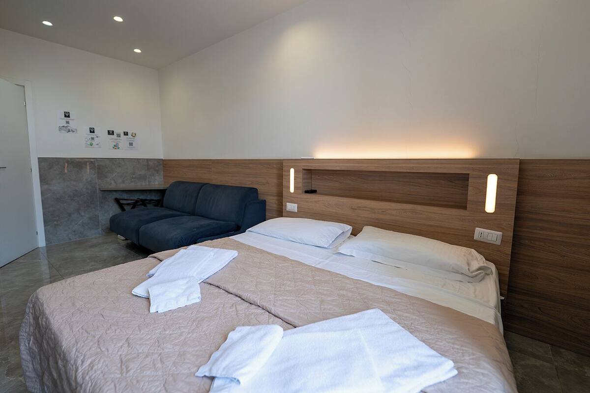 A modern hotel room with a large bed, a sofa, and a small seating area.