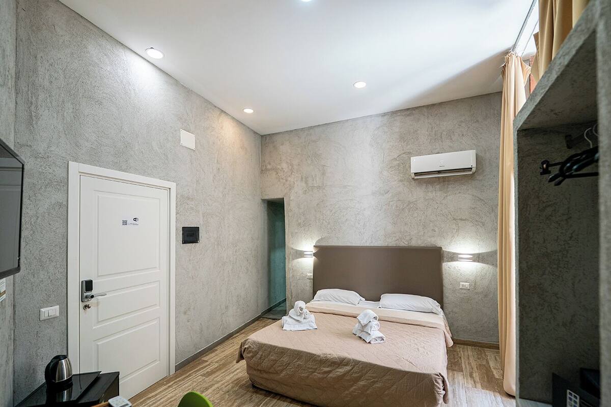 A bedroom with a bed, a door, a wall-mounted air conditioner, and a small table with a kettle.