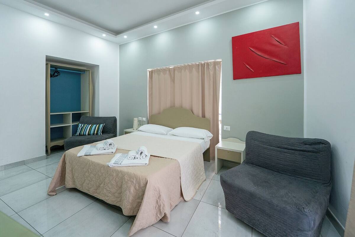 A hotel room with a bed, a chair, a desk, and a wardrobe.