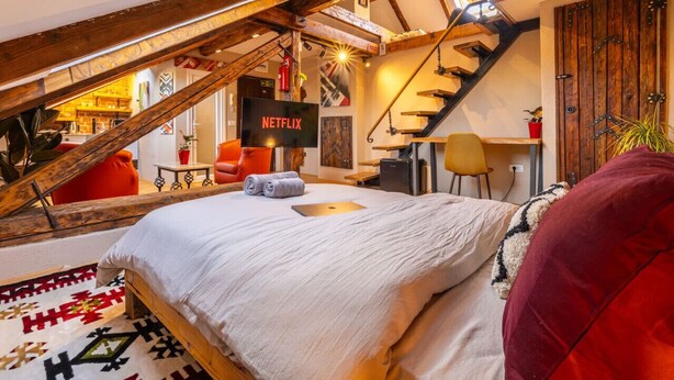 Un dormitorio estilo loft acogedor con techo inclinado, una cama, un escritorio y un televisor mostrando el logotipo de Netflix.