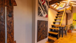Una escalera de madera de estilo rústico, una puerta de madera con herrajes metálicos y una obra de arte colgada en la pared.
