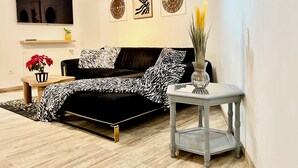 Un salon moderne avec un canapé noir, un plaid à motifs, une petite table d’appoint surmontée d’un vase et des œuvres d’art décoratives accrochées au mur.