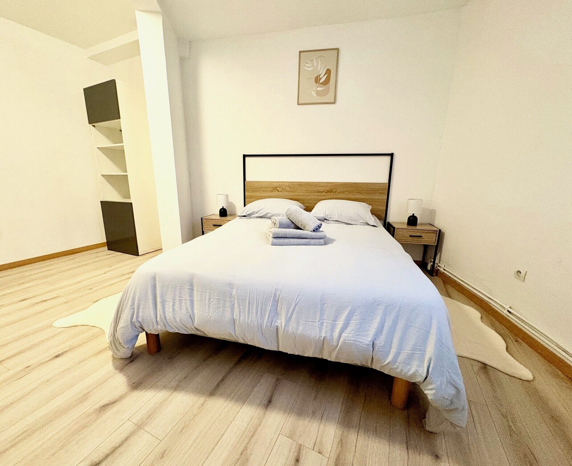 Een netjes opgemaakt bed met een houten hoofdbord, een nachtkastje met een lamp en een aan de muur hangend schilderij.