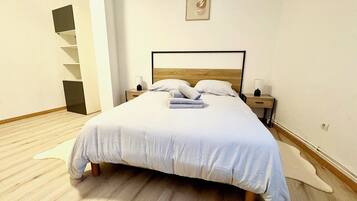 Een netjes opgemaakt bed met een houten hoofdbord, een nachtkastje met een lamp en een aan de muur hangend schilderij.