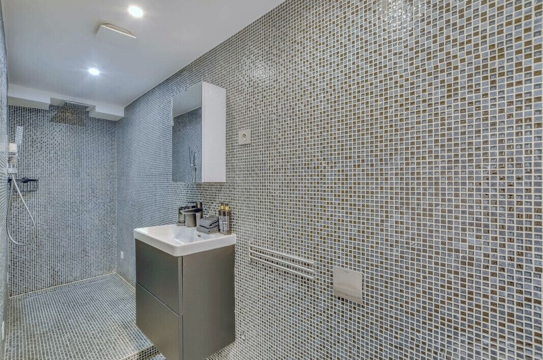A bathroom with a tiled wall, a sink, and a mirror.