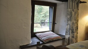 Una ventana pequeña con una reja de hierro decorativa, un cojín y una cortina de estampado tradicional.