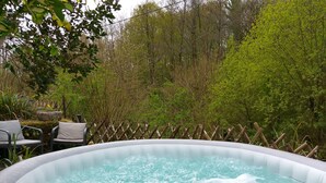 Un jacuzzi al aire libre rodeado por una valla de madera, con sillas y una maceta de piedra cerca.