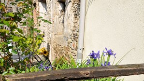 Pared de piedra con una tubería, rodeada de follaje y flores.