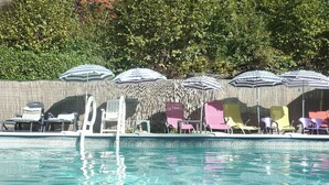 Piscina con sillas de descanso y sombrillas, rodeada por una valla de madera y follaje.