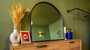 A wooden dresser with a large mirror, a vase with dried plants, a framed picture, and a small clock on the wall. - SquareView Apartment (Prishtina)
