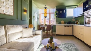 A modern living room with a sofa, a coffee table, and a dining area with chairs and a table. - SquareView Apartment (Prishtina)
