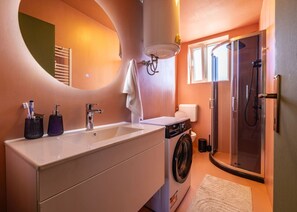 Une petite salle de bain comprenant un lavabo, un lave-linge et une douche à parois en verre.