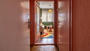 Un pasillo con piso de madera que conduce a una habitación con alfombra colorida, una pequeña mesa y una lámpara colgante.