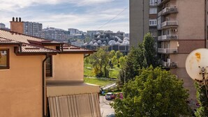 Un edificio residencial con balcón, antena parabólica y vistas a un parque con árboles y un paisaje urbano distante.