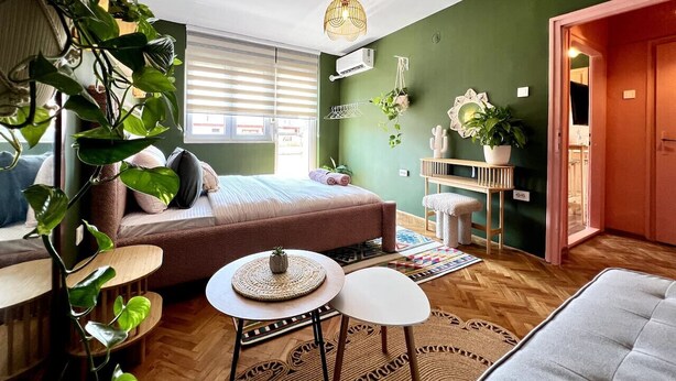Un dormitorio acogedor con cama, mesita de noche, planta colgante y ventana con persianas.