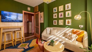 Una sala de estar acogedora con un sofá, un televisor, una mesita y una pared decorada con cuadros.