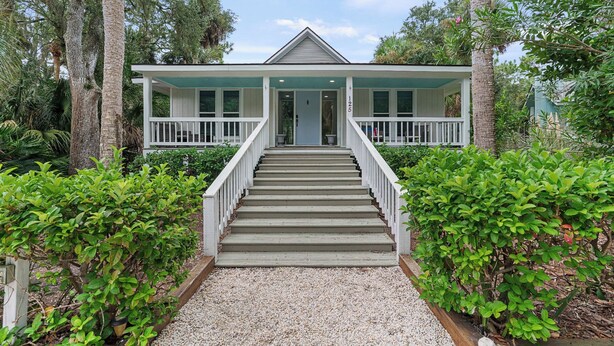 Ein zweistöckiges Haus mit Veranda, einer Treppe zum Eingang und einem gepflegten Garten.