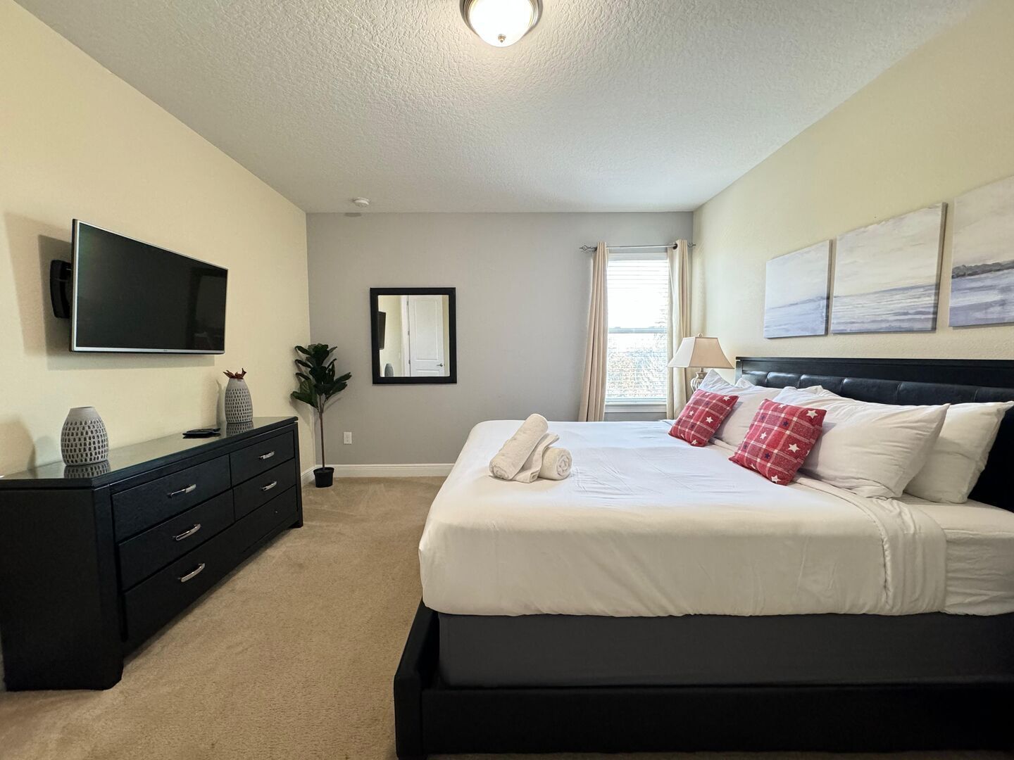 A bedroom with a bed, a dresser, a TV, a mirror, and artwork on the wall.