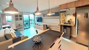 A modern kitchen with a central island, stainless steel appliances, pendant lighting, and a view to the outside. - Aloha Residence (Ipojuca)