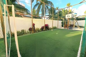 Une cour arrière clôturée avec une pelouse artificielle, un panier de basketball et une petite structure de jeux.