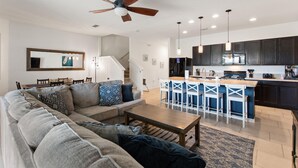 A modern living room with a sofa, coffee table, and a kitchen area with bar stools. - 25% Off Luxury Disney Retreat in Solterra (Davenport)
