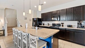 A modern kitchen with dark wood cabinets, a granite countertop, a central island with bar stools, and pendant lighting. - 25% Off Luxury Disney Retreat in Solterra (Davenport)