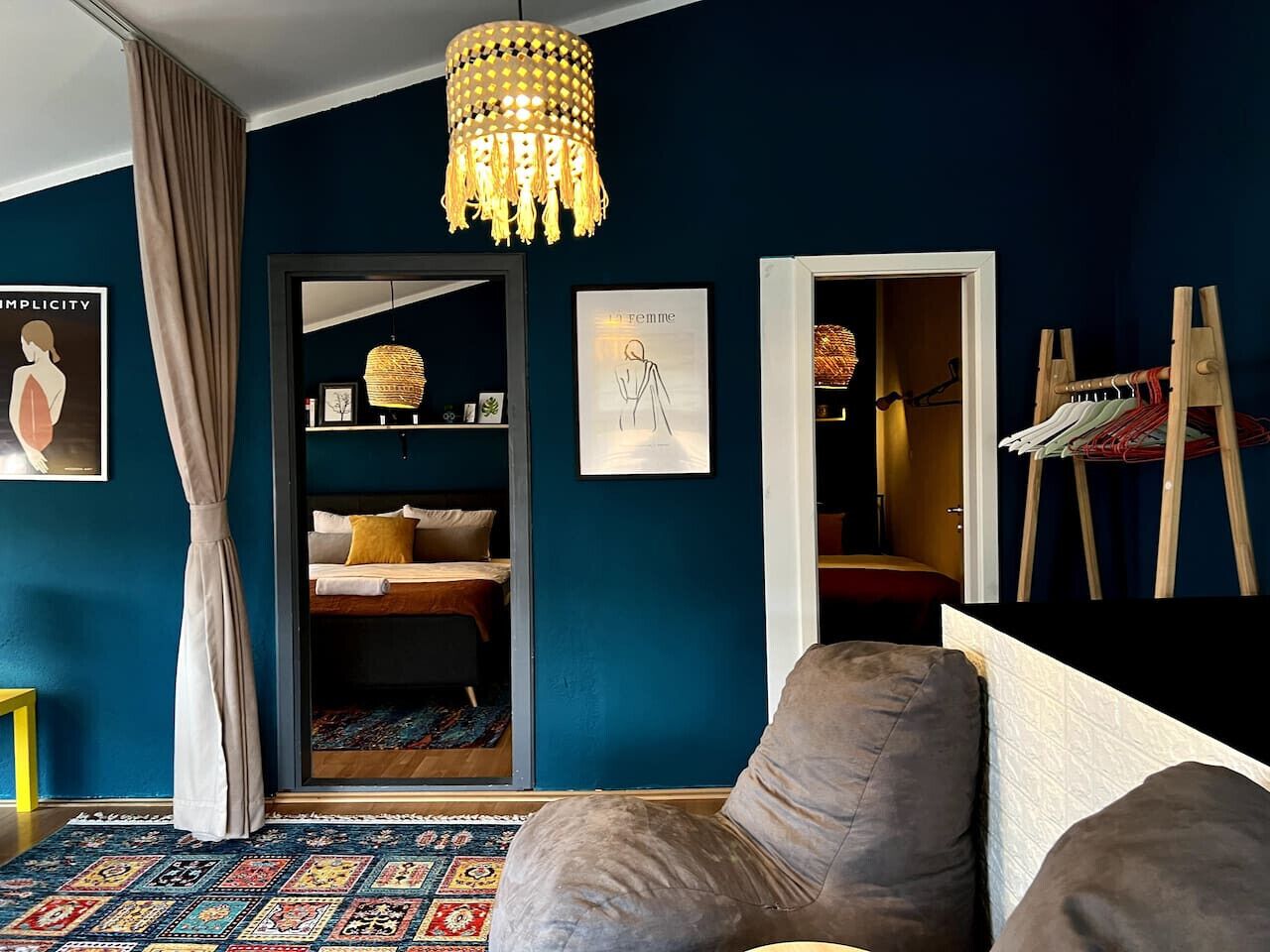 A room with a blue wall, a large window, a bed with a patterned rug, a hanging light fixture, and a framed artwork.