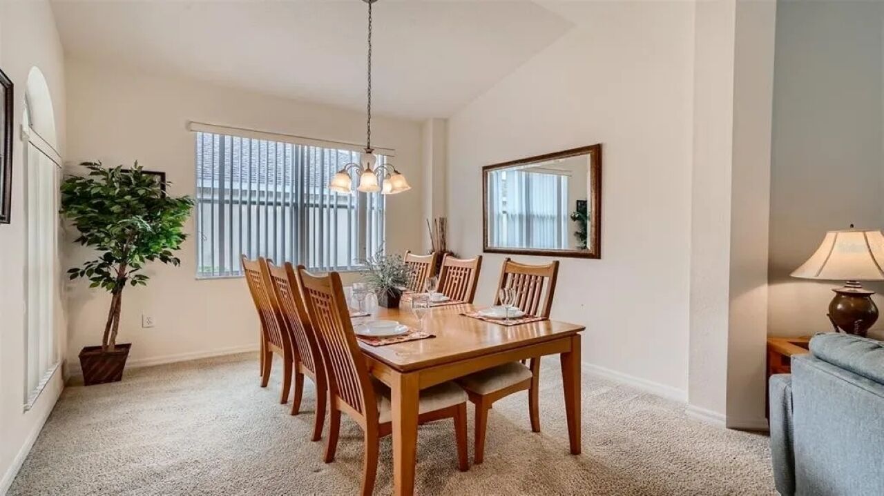 A dining room with a wooden table and chairs, a hanging light fixture, a potted plant, and a mirror on the wall.