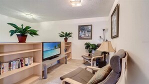 Una sala de estar con televisor, estanterías, un sofá y dos plantas en macetas.