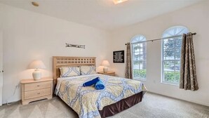 Un dormitorio con una cama de madera, dos mesitas de noche con lámparas, un ventanal con cortinas y una pared decorada con una cita.