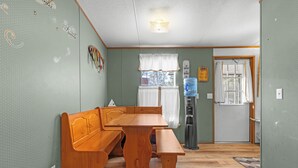 Une pièce comprenant un banc et une table en bois, un distributeur d’eau et une porte avec une fenêtre.