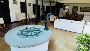 A spacious lobby with a central round table featuring a decorative wheel, surrounded by seating areas and a large window offering a view. - HOTEL CAFELIA BOUTIQUE (Pereira)