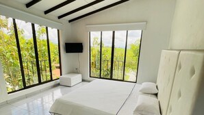 A modern bedroom with a large bed, a TV, and large windows offering a view of greenery. - HOTEL CAFELIA BOUTIQUE (Pereira)