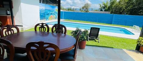 Eine überdachte Terrasse mit Pool, Esstisch und Stühlen.