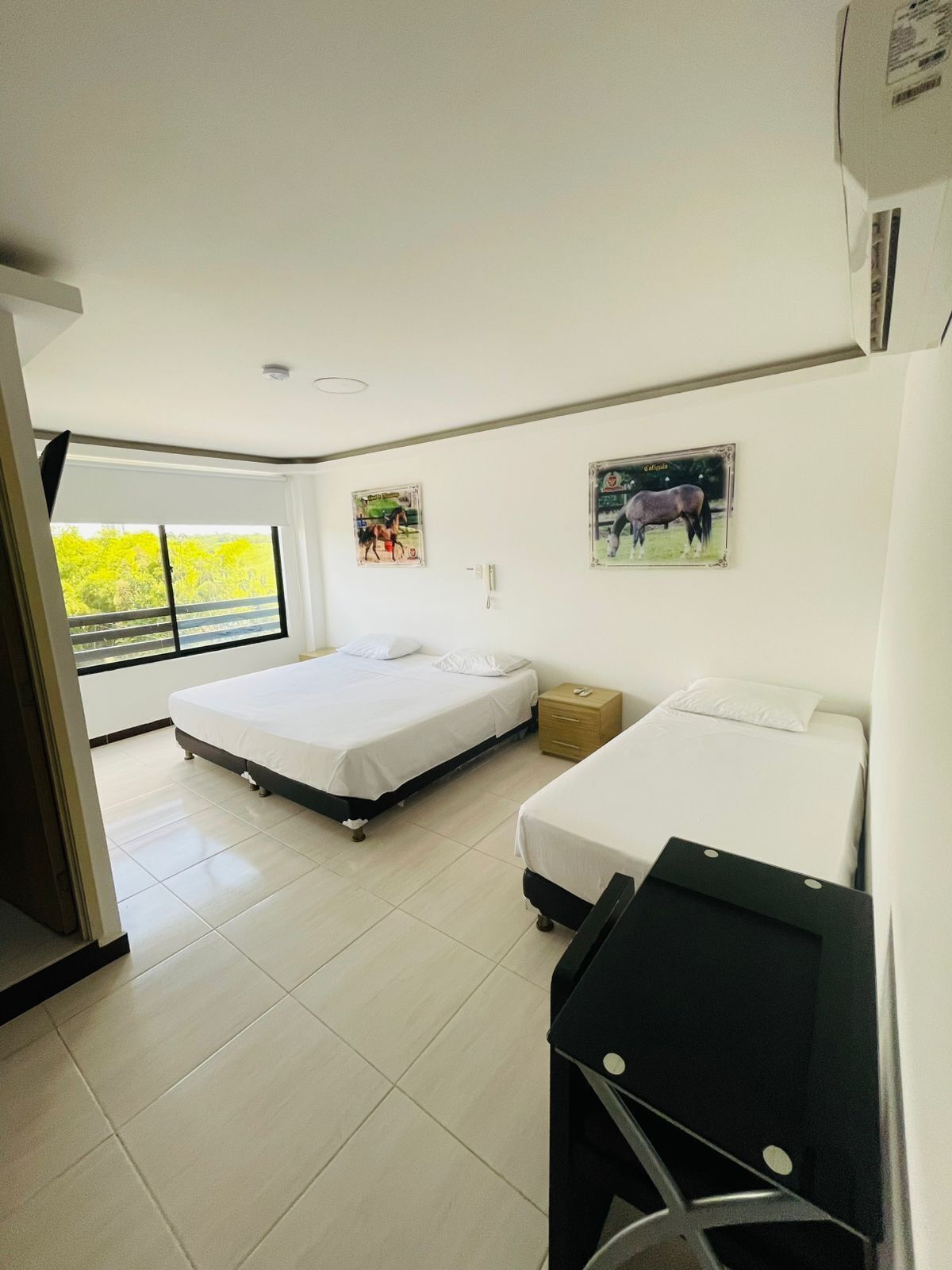 Habitación de hotel con dos camas, un escritorio y una ventana con vistas a zonas verdes.