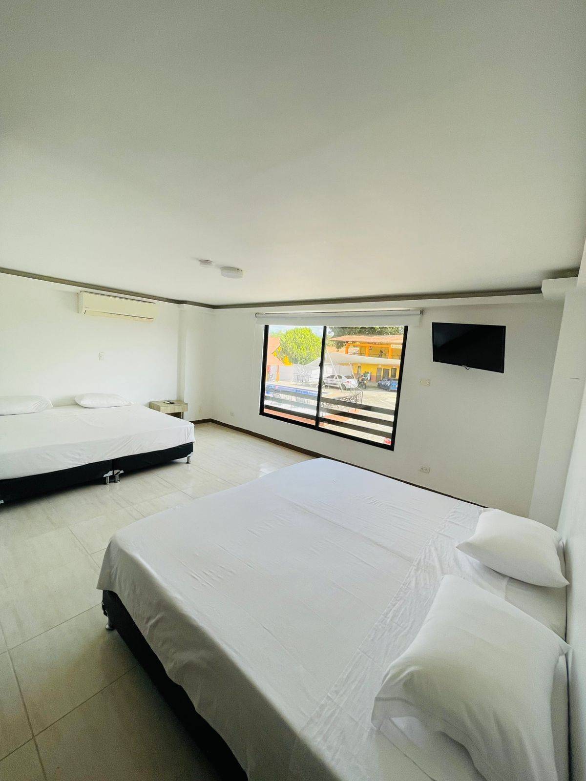 A hotel room with two beds, a TV, and a window with a view of the outside.