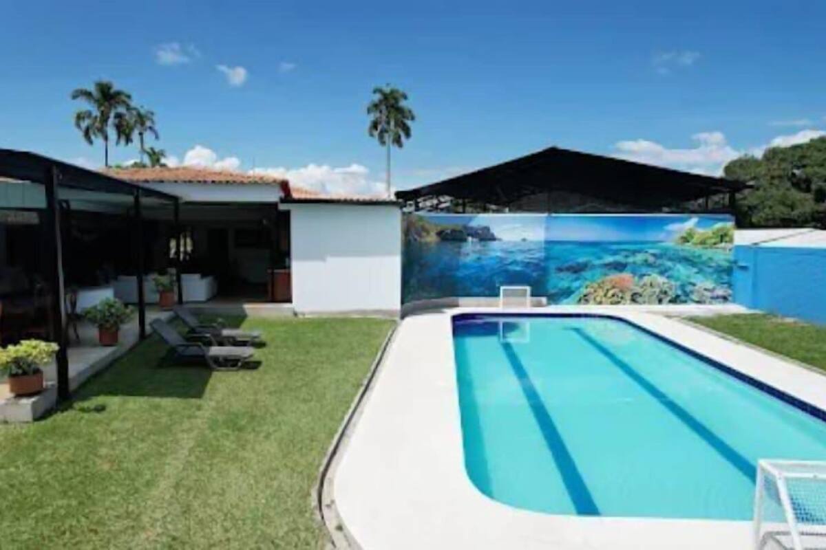 Una piscina con un fondo de mural tropical, un patio cubierto y un césped bien cuidado.