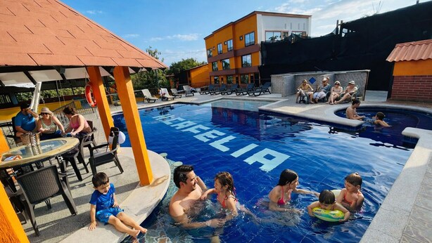 A swimming pool with the word "REELIA" on the water, surrounded by lounge chairs and a covered seating area. - HOTEL CAFELIA BOUTIQUE (Pereira)