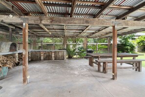 An outdoor covered patio with concrete flooring, wooden benches, and a rustic wooden structure with a corrugated metal roof. - Rawsons Escape Country Comfort by Coledale Beach (Coledale)