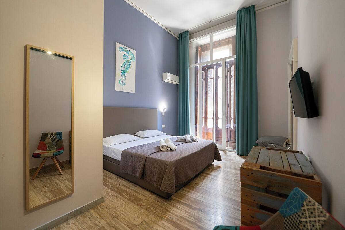A hotel room with a bed, a chair, a desk, a TV, and a window with curtains.