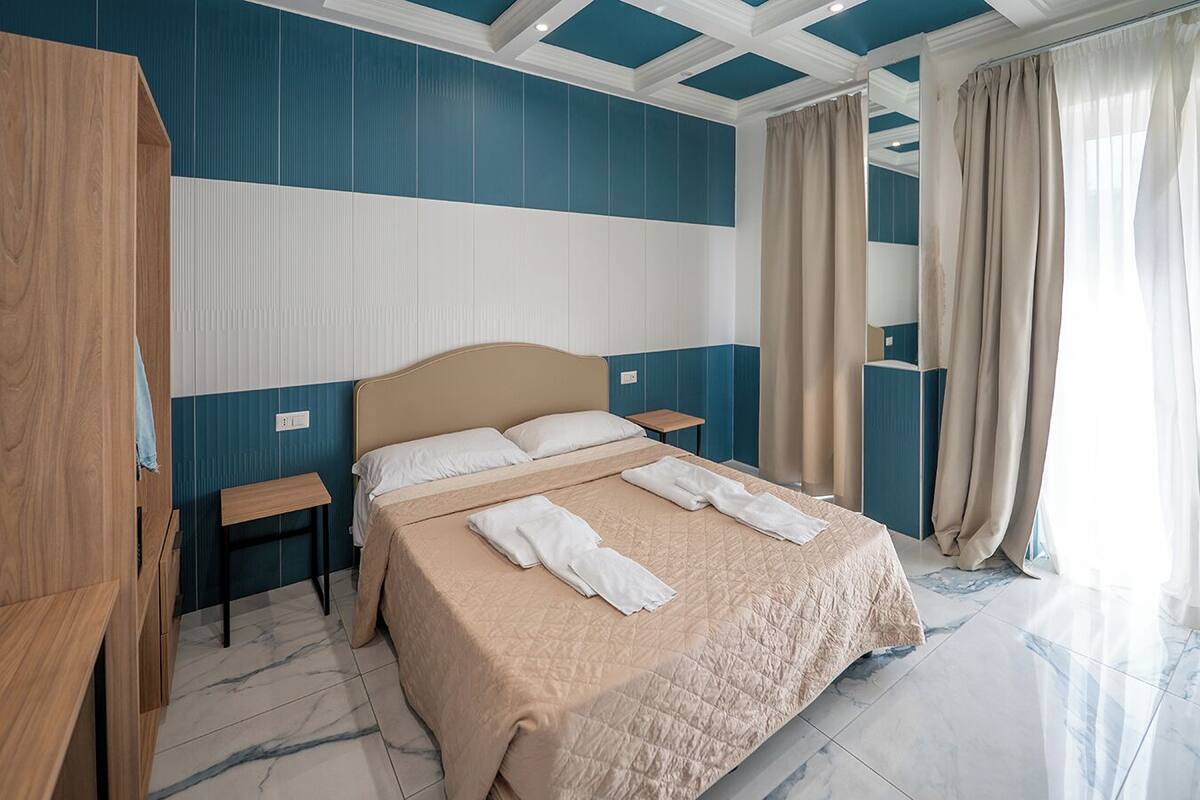 A hotel room with a large bed, two bedside tables, a wooden wardrobe, and a bathroom with a bathtub.