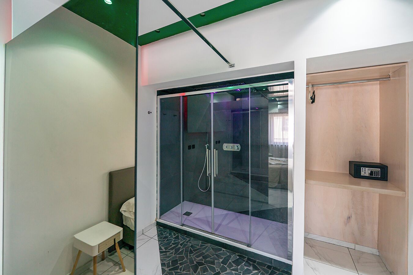 Een moderne badkamer met een douchecabine van glas, een klein nachtkastje en een houten plank.