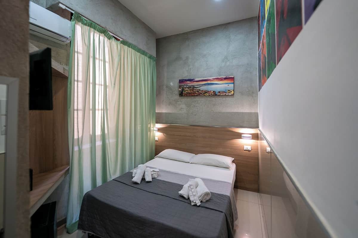 A hotel room with a bed, a painting on the wall, and a TV mounted on the wall.