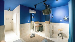 A modern bathroom with blue walls, a large mirror, a television, and a small stool. - GREROS H. HISTORICAL AREA, by Clapa Group dislocated hospitality Acquisition (Naples)