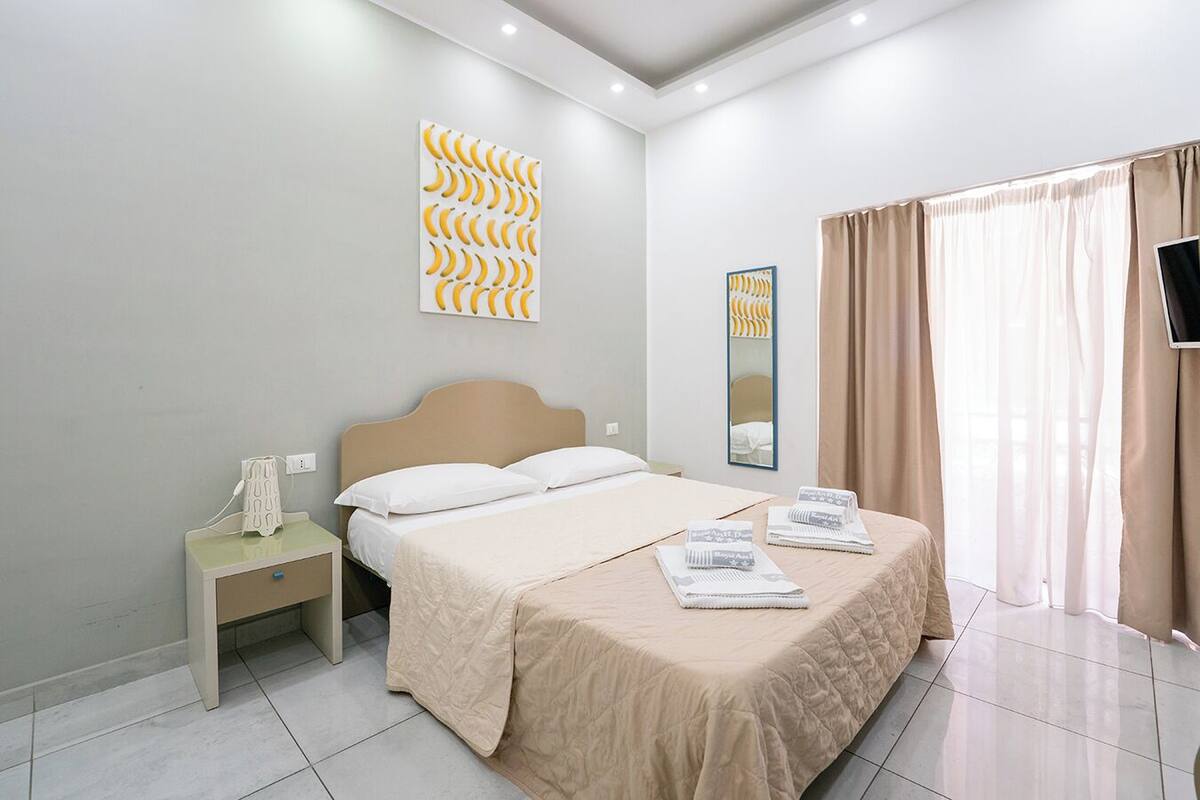 A modern hotel room with a bed, bedside table, and a large window with curtains.