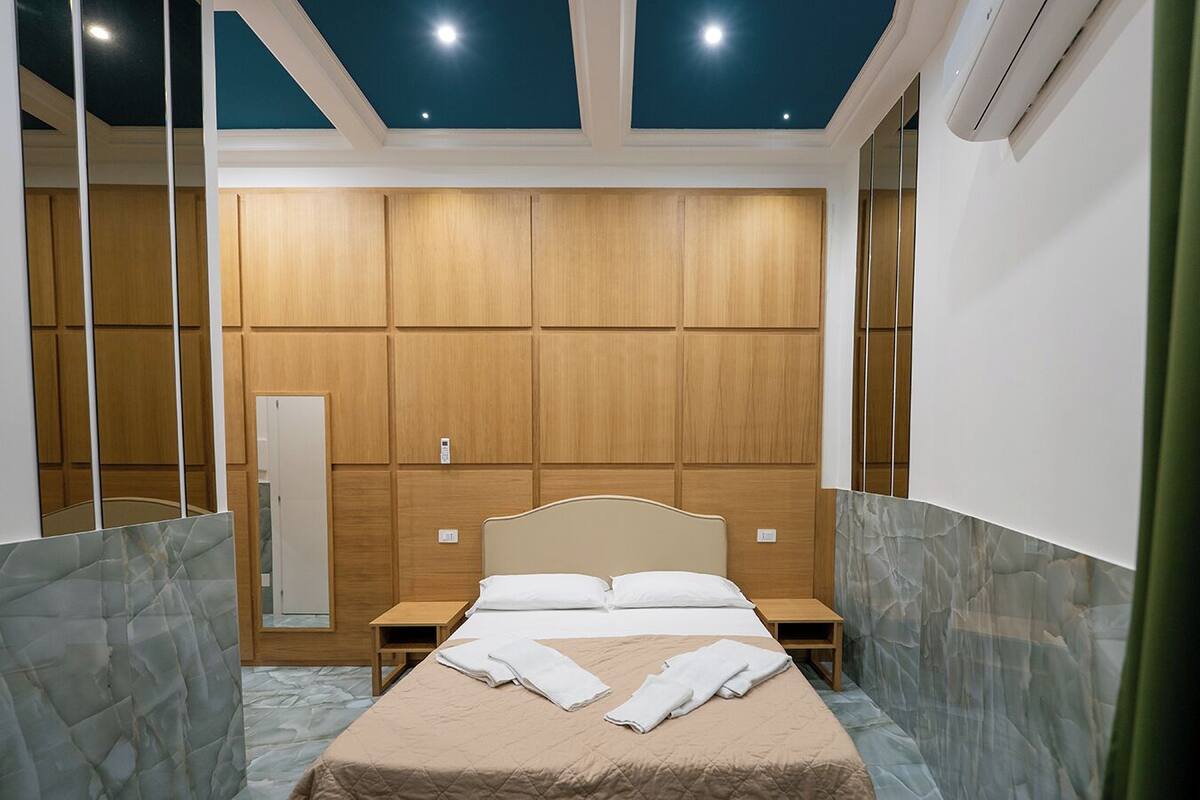 A bedroom with a bed, nightstands, a mirror, and a wooden panel wall.