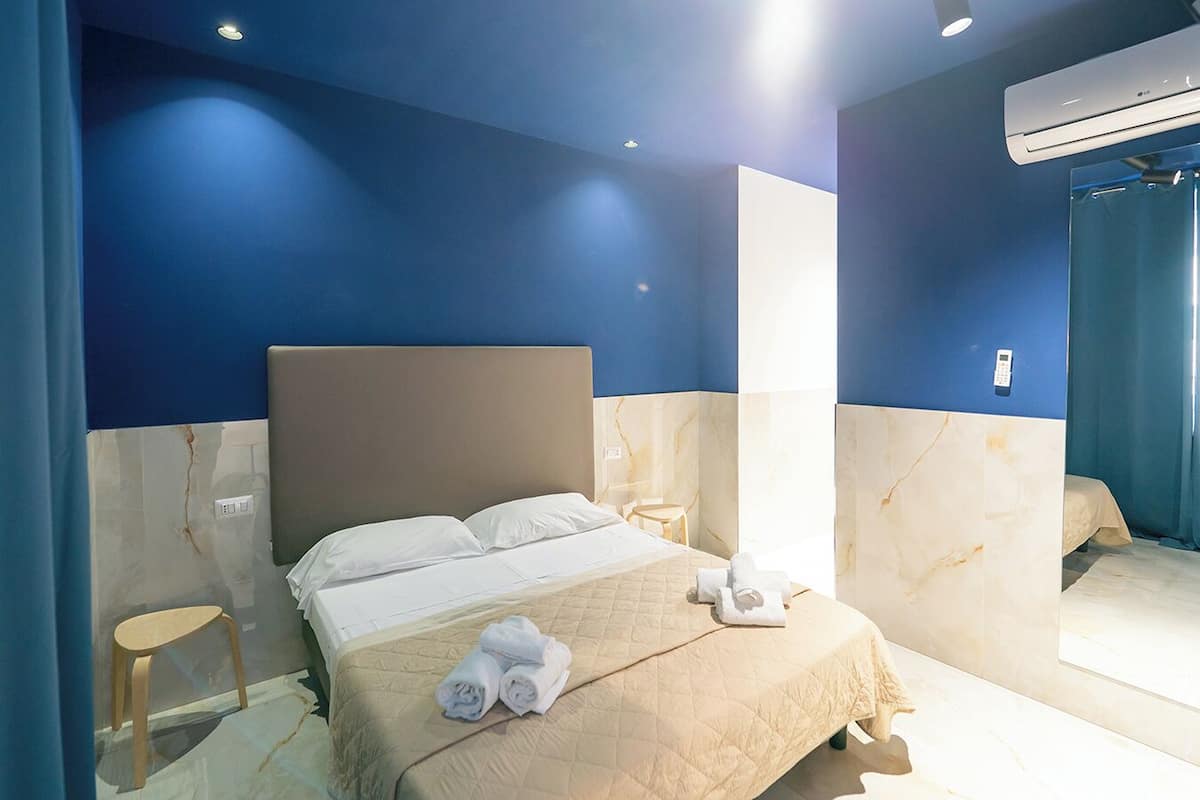 A modern hotel room with a large bed, a bedside table, a chair, and an air conditioning unit.