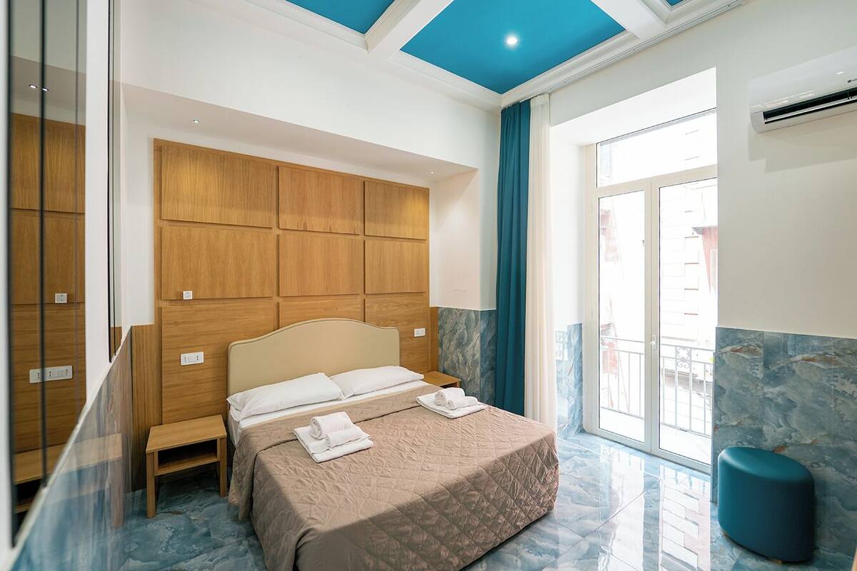 A hotel room with a bed, wooden wardrobe, and a balcony with a view.