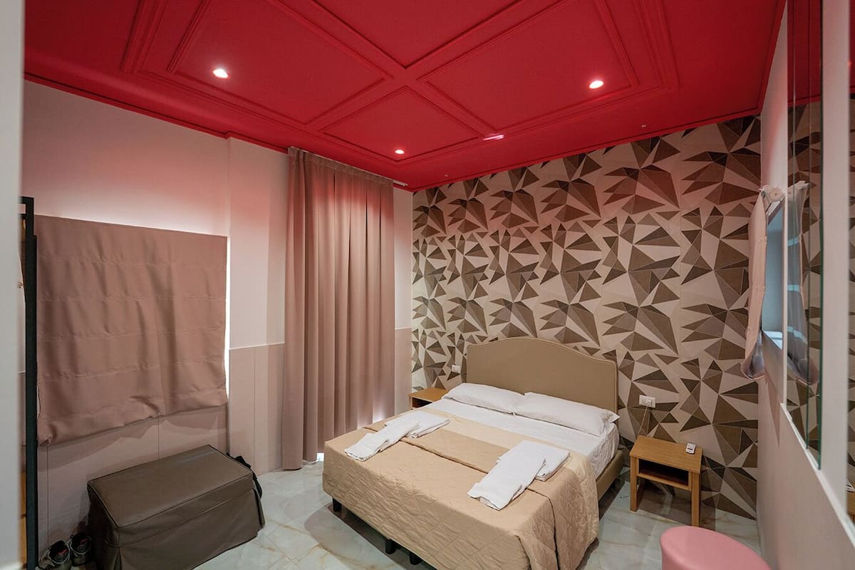 A hotel room with a bed, a bench, a small table, a suitcase, and a mirror.